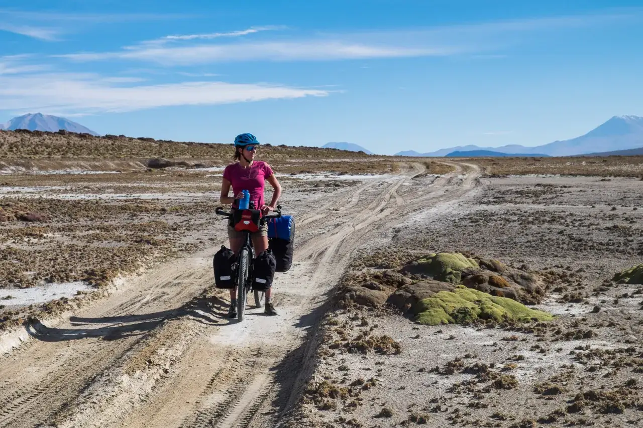 Kobieta na rowerze z sakwami na pustkowiu. To krajobraz, z którego słynie Boliwia – surowy, ale piękny.