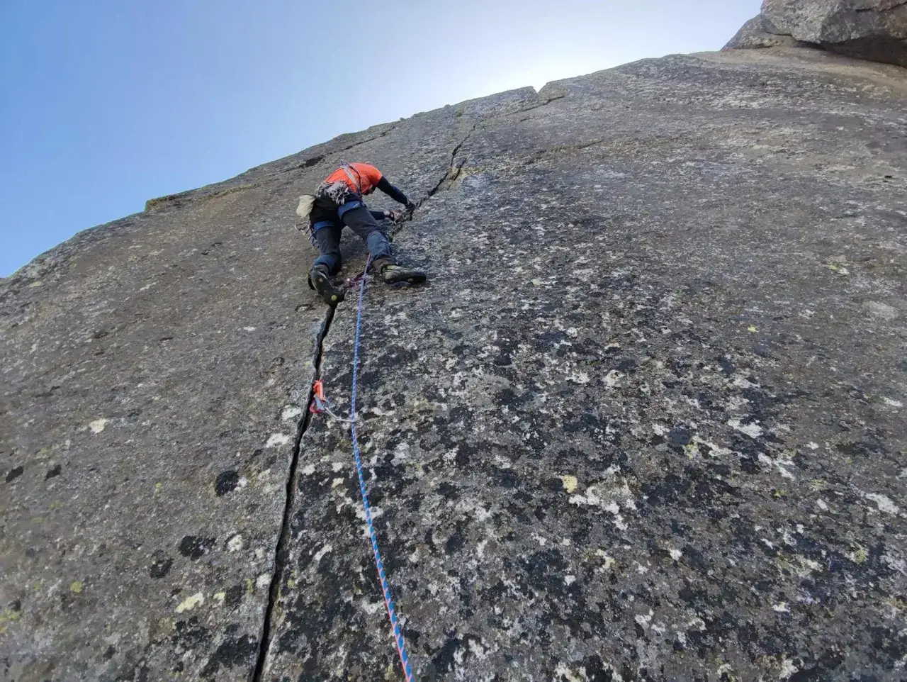 Wspinacz pokonuje trudną drogę, oceniając każdy chwyt na skale. To wyzwanie na skalę taternicką, wymagające precyzji i siły.
