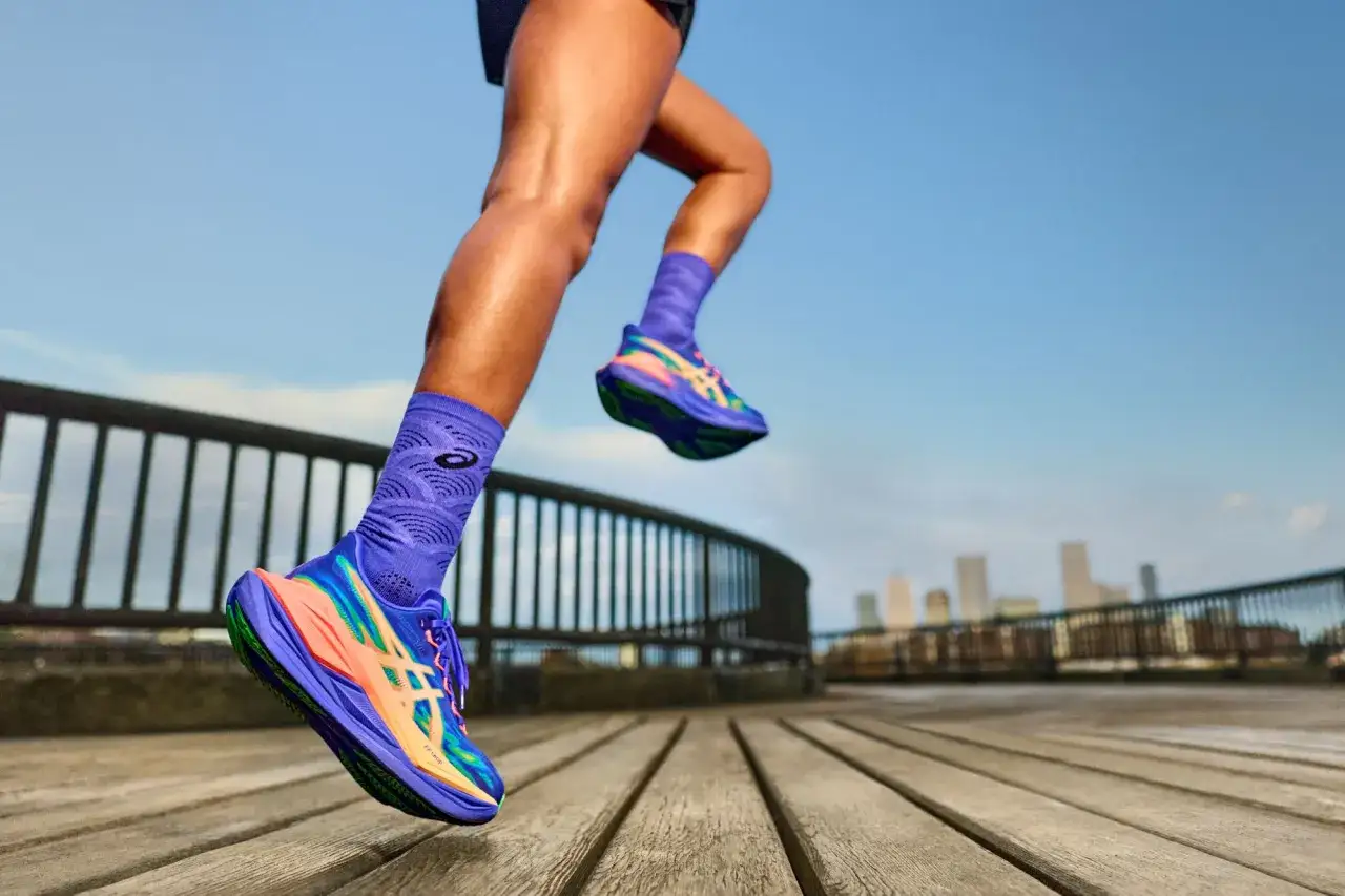 Nogi biegacza w kolorowych butach Asics Running i fioletowych skarpetkach na drewnianym tarasie z widokiem na miasto.