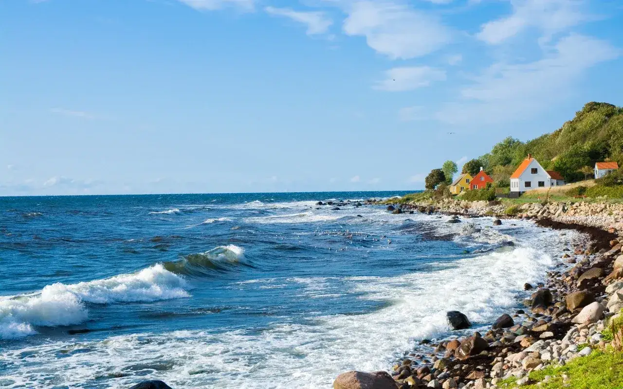 Malownicze domki na wzgórzu nad Bałtykiem. Falująca woda i kamienista plaża tworzą sielski krajobraz duńskiej wyspy.