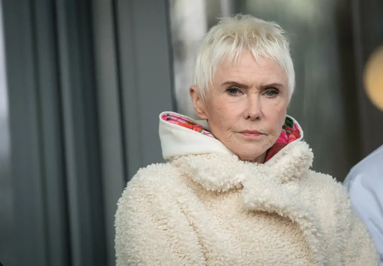 Ewa Błaszczyk w białym, barankowym płaszczu, z krótkimi blond włosami. W jej oczach widać smutek po stracie, bo córka Ewy Błaszczyk nie żyje.