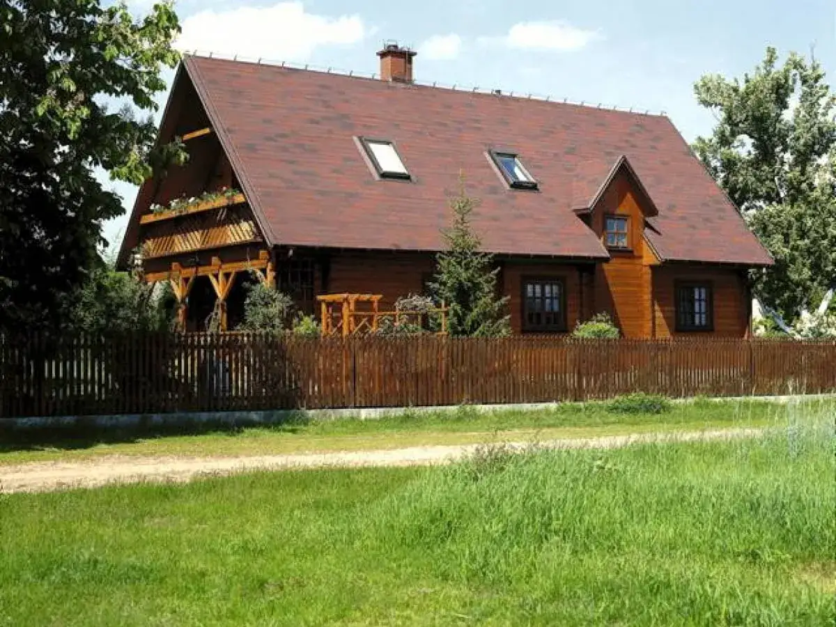 Drewniany dom z werandą i drewnianym płotem. Taka zabudowa zagrodowa może być budowana przez rolnik&oacute;w na ich gruntach.