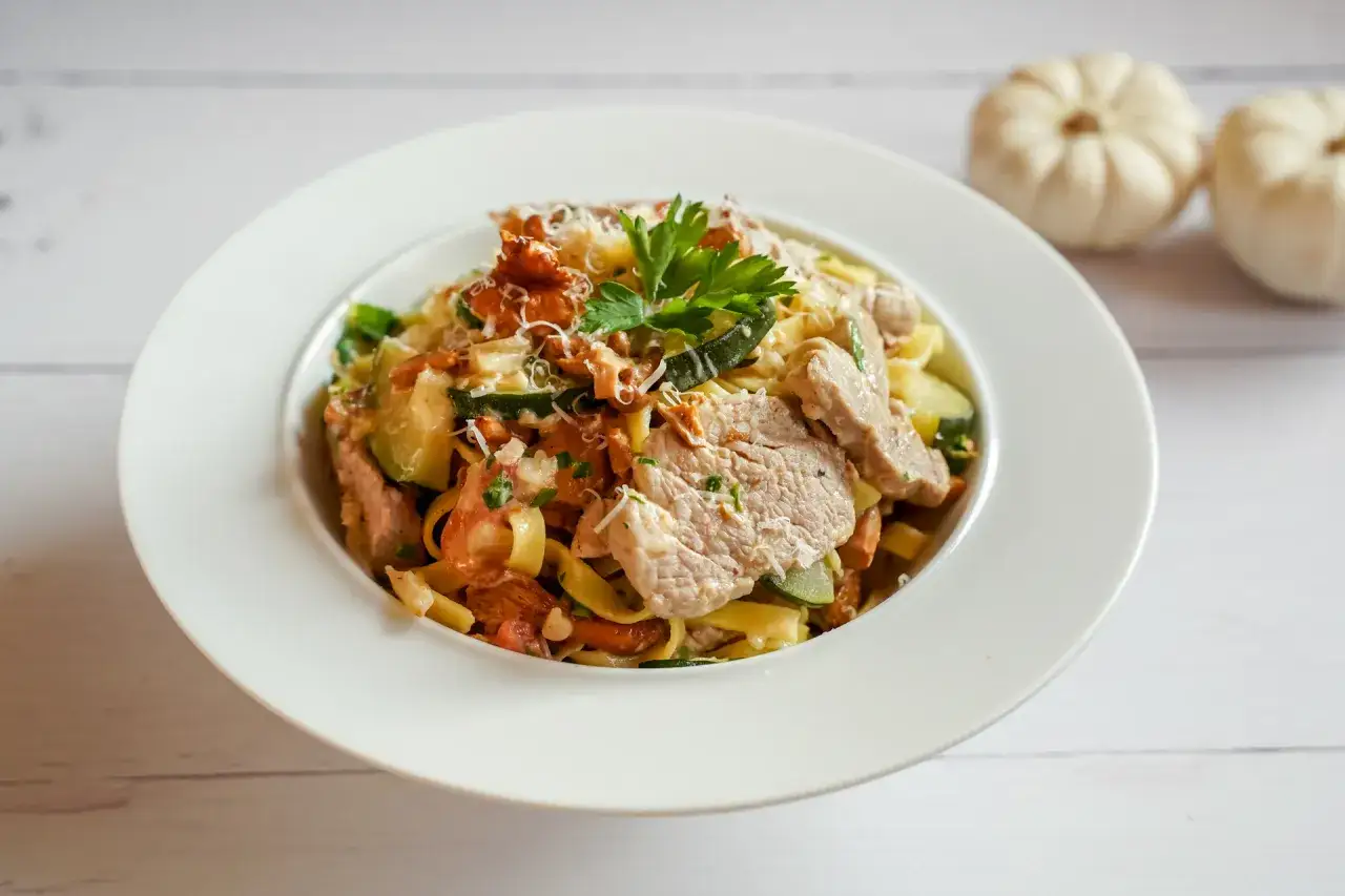 Pyszny makaron z polędwiczką, cukinią i parmezanem, udekorowany natką pietruszki.