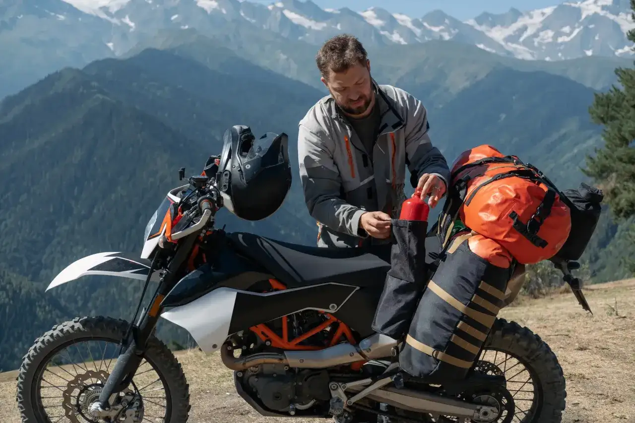 Mężczyzna przygotowuje motocykl do wyprawy, sprawdzając, co zabrać na wyprawę motocyklową. W tle góry.