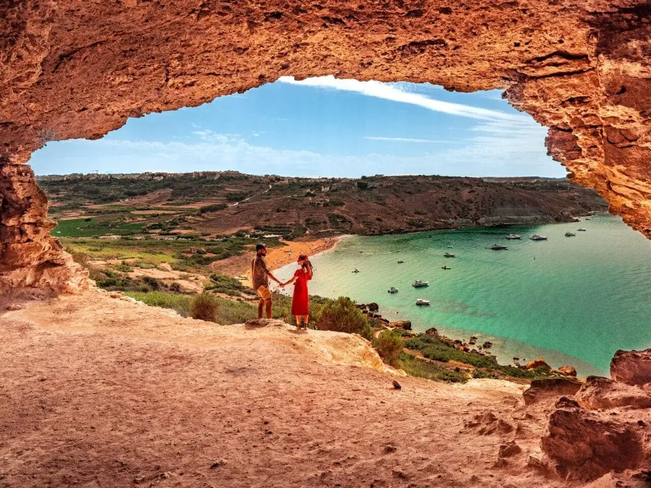 Para co robić na Malcie w lutym? Spacer po jaskini z widokiem na zatokę z łodziami i parą zakochanych.