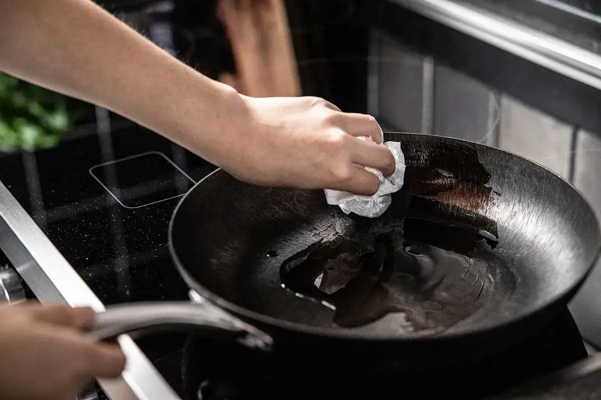 Ręka wciera olej w patelnię żeliwną, przygotowując ją do pierwszego użycia. To kluczowy krok, jak przygotować patelnię żeliwną.
