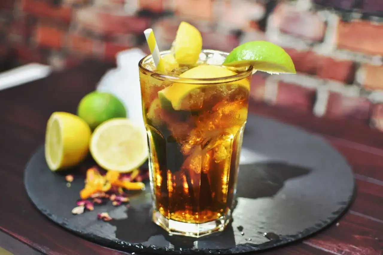 Orzeźwiający long island iced tea z cytryną i limonką, podany z lodem i słomką, na tle ceglanej ściany.