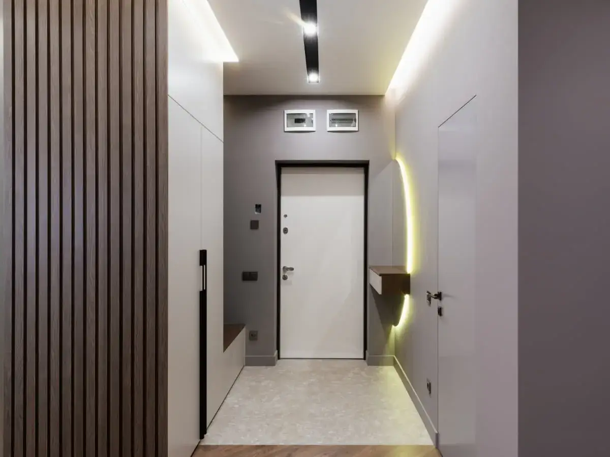 Nowoczesne oświetlenie i drewniane panele pomagają rozjaśnić wąski korytarz, tworząc przytulną atmosferę.