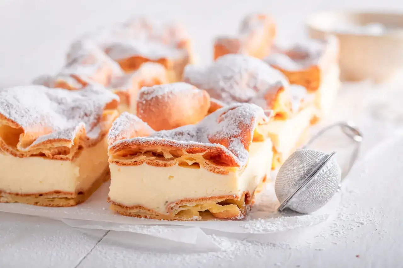 Pyszna karpatka bezglutenowa, opr&oacute;szona cukrem pudrem, wygląda apetycznie. Idealna na deser, gdy szukasz przepisu bez glutenu.