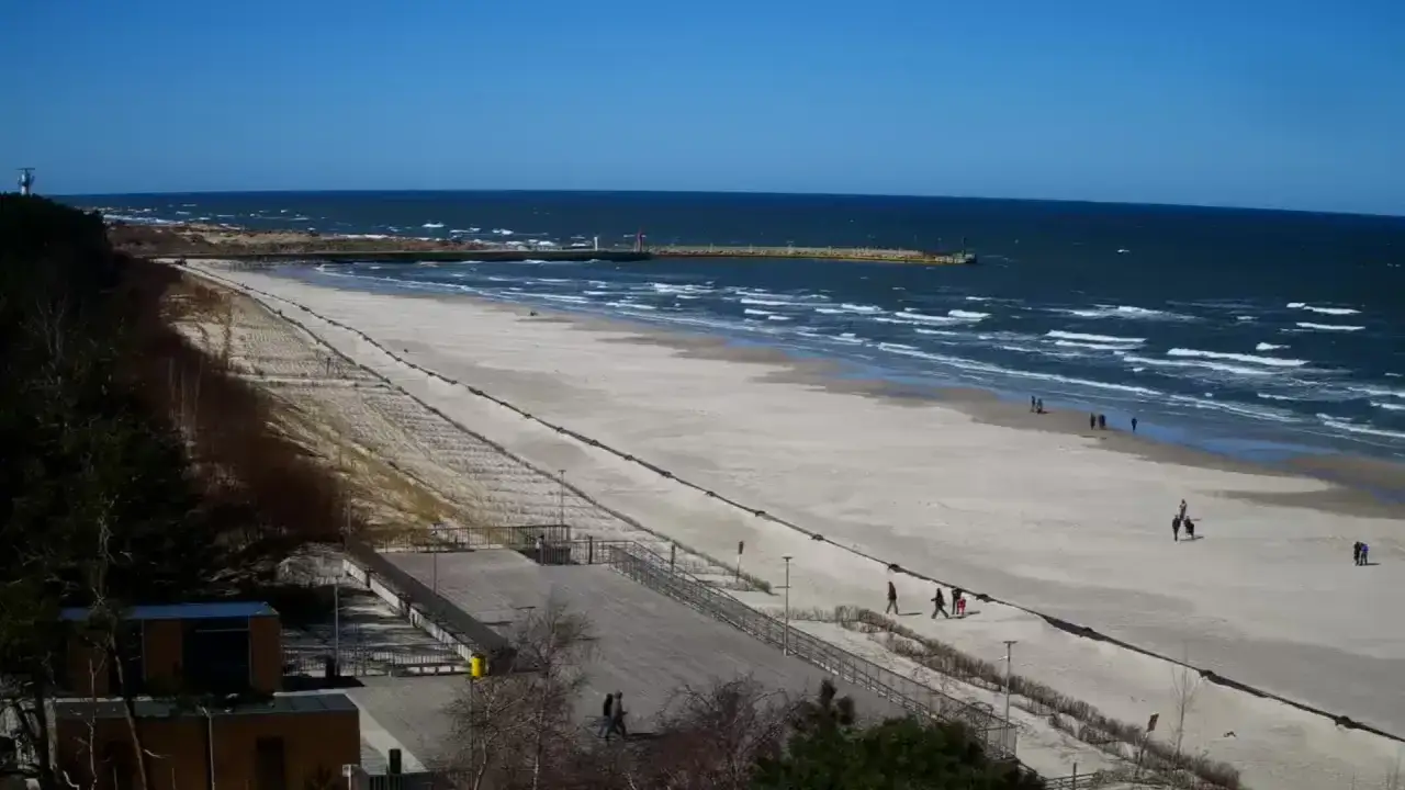 Spacerem po plaży zachodniej Łeby, widać falujące morze i kilka osób spacerujących po piasku.