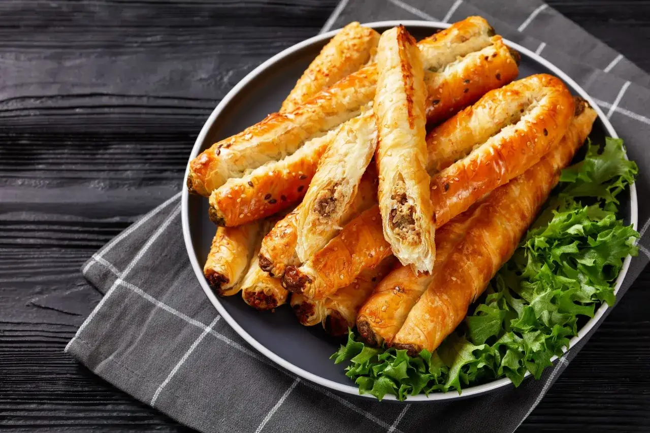 Złociste, chrupiące ciasto filo na słono, nadziewane mięsem, posypane sezamem. Podane na talerzu z sałatą.