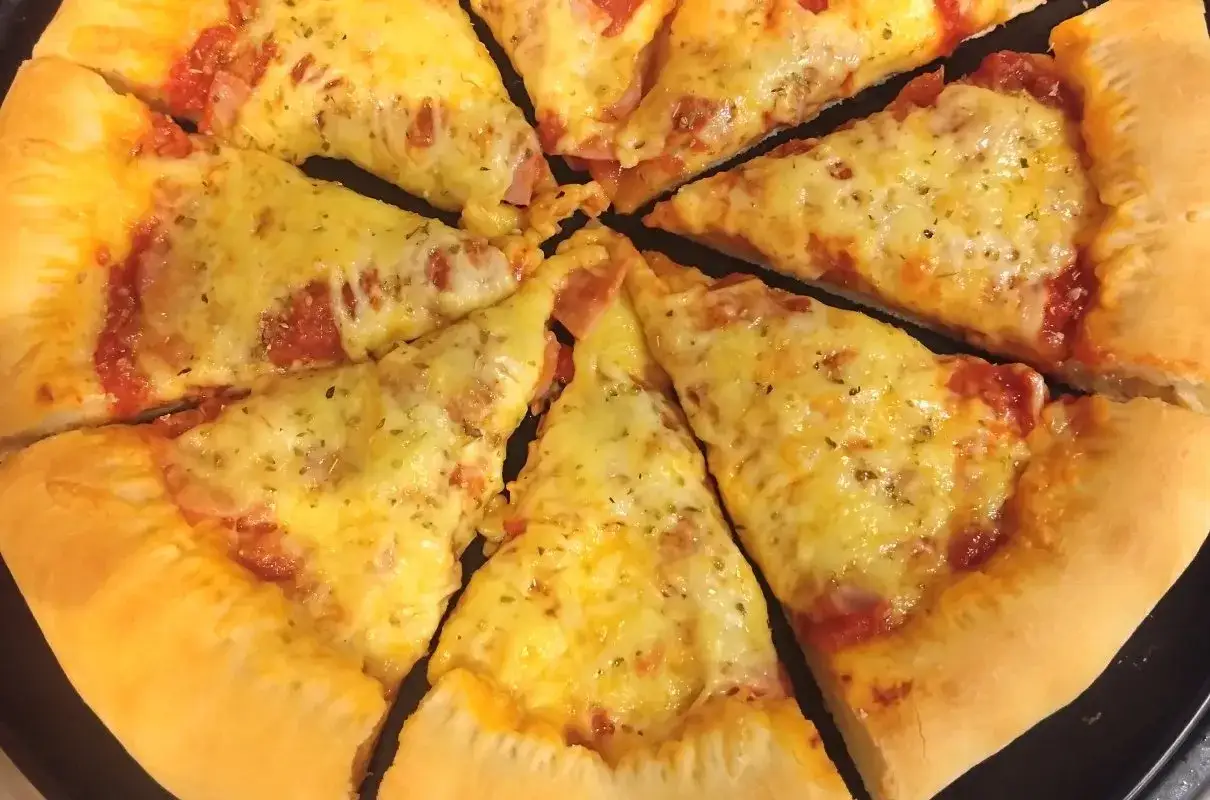 Pyszna pizza z grubym ciastem, obficie posypana serem i ziołami, pokrojona na kawałki.