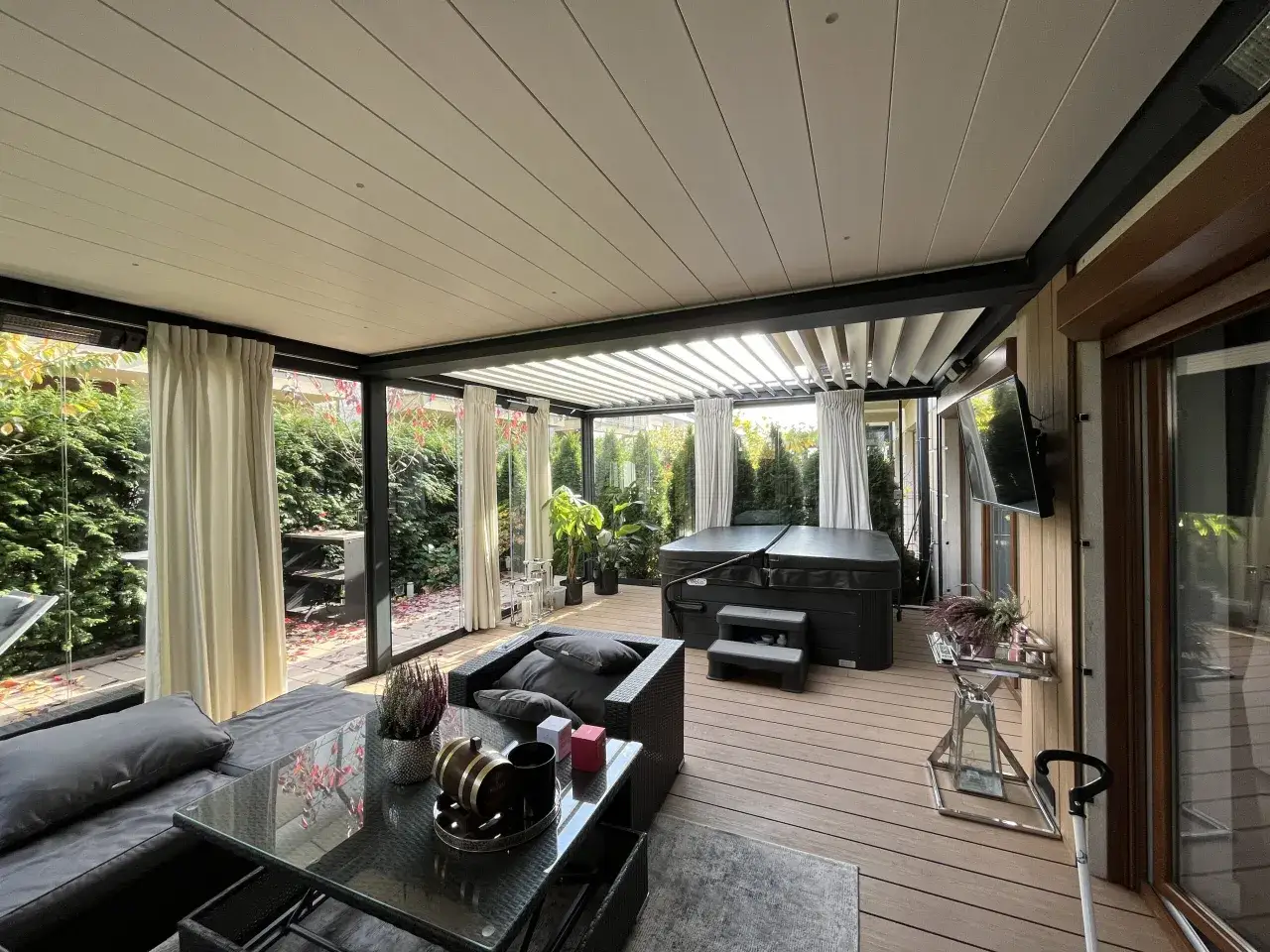 Nowoczesna weranda z jacuzzi, sofą i stolikiem kawowym. Otoczona zielenią, idealna do relaksu.