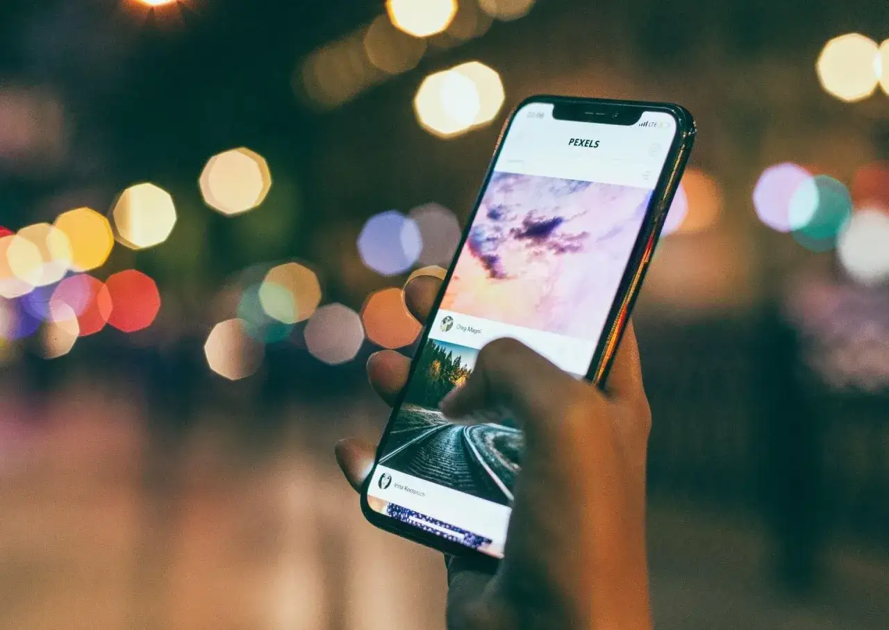 Dłoń trzyma iPhone'a z widokiem na Pexels. Zastanawiasz się, jak namierzyć iPhone po IMEI?