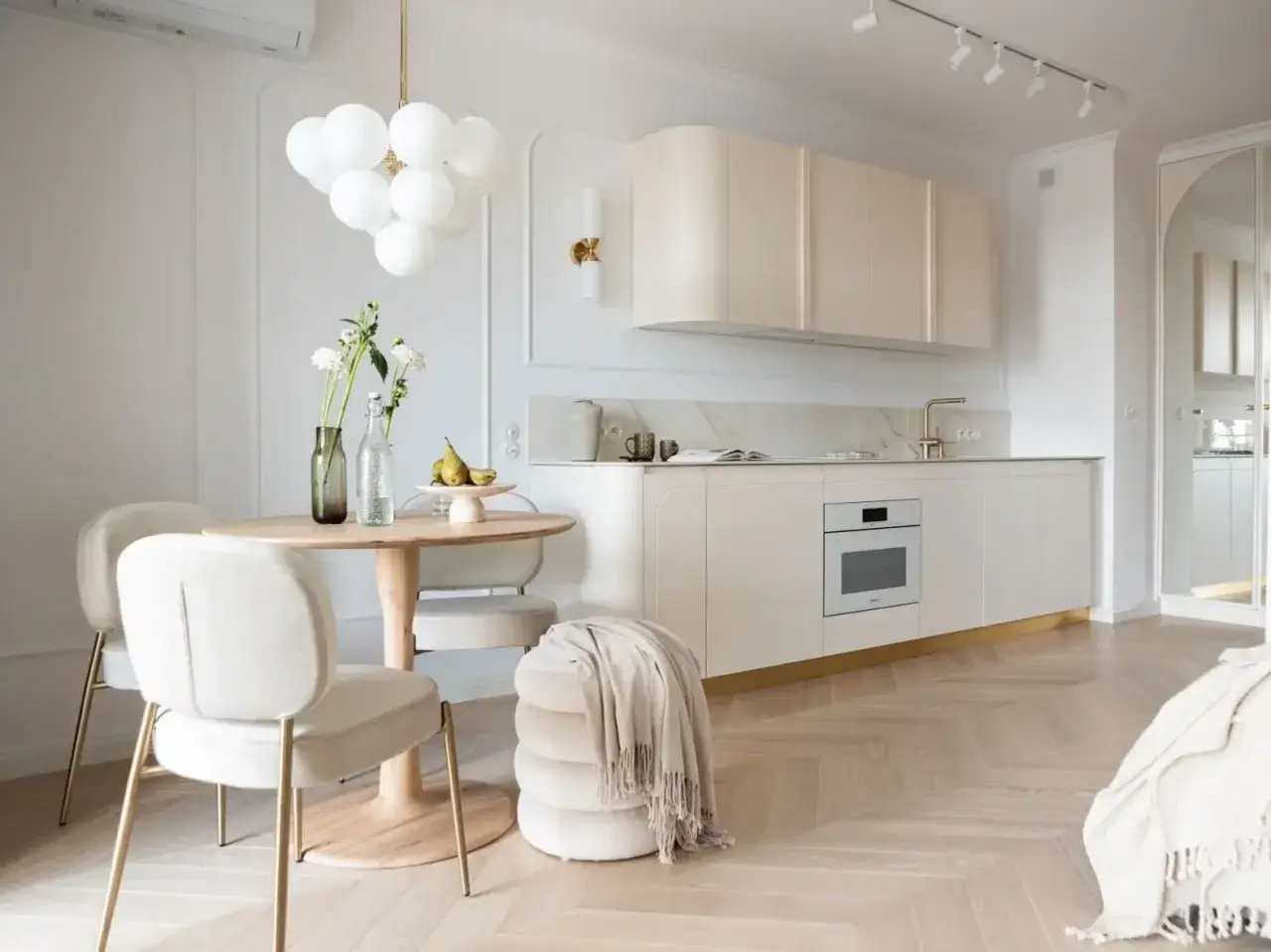 Okrągły stół z krzesłami i lampa do jadalni nad stół. W tle nowoczesna kuchnia z białymi meblami i złotymi akcentami.