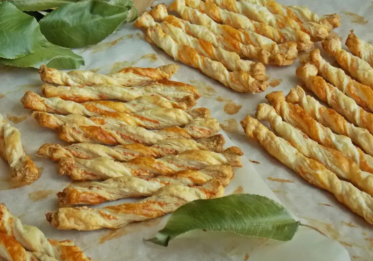 Chrupiące paluchy z ciasta francuskiego, lekko zarumienione, ułożone na papierze do pieczenia.