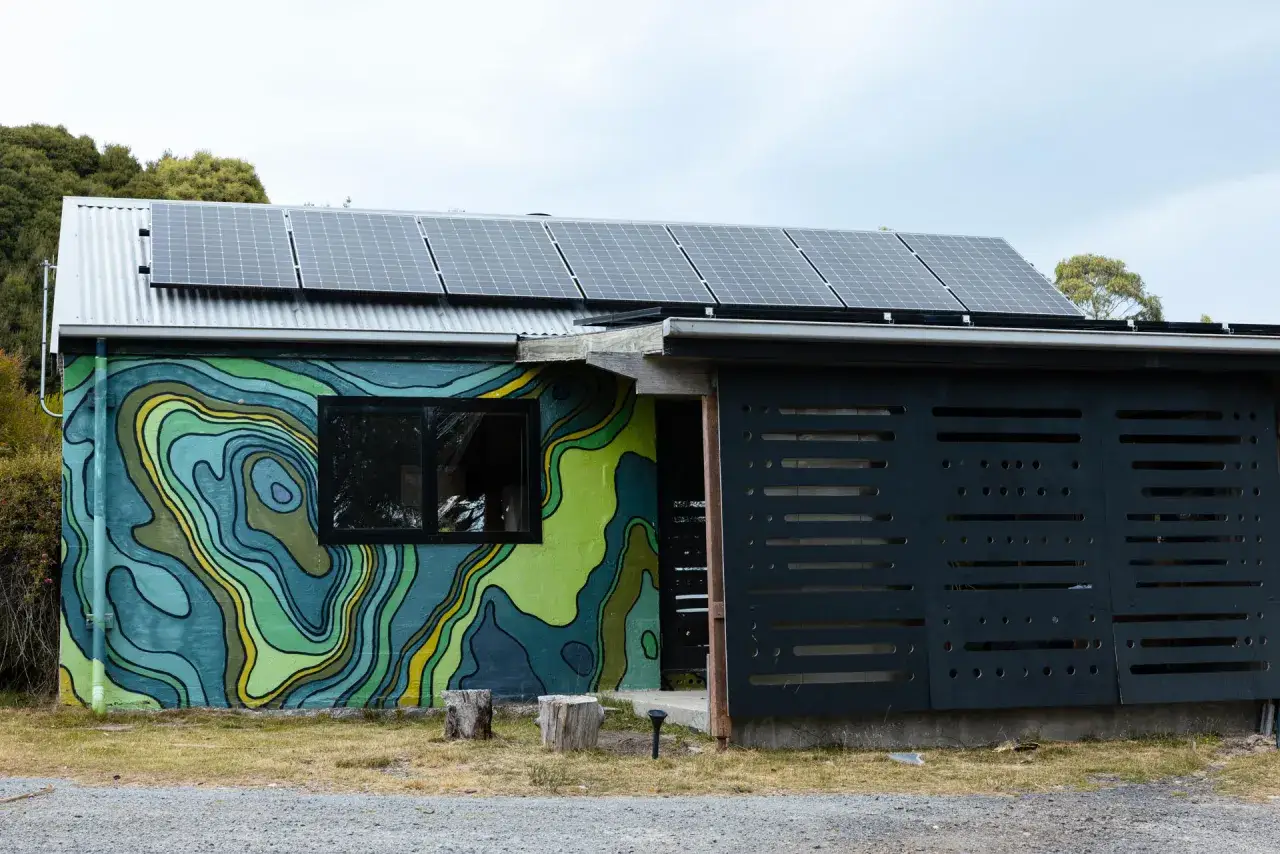 Dom z muralem w kształcie mapy topograficznej, panele słoneczne na dachu i czarna, ażurowa ściana z otworami tworzącymi wz&oacute;r **grid**.