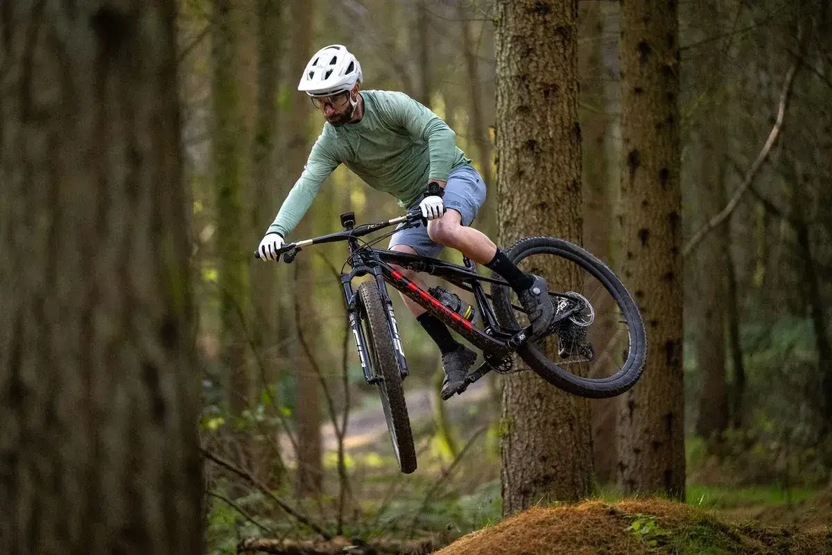 Kolarz w kasku skacze na rowerze MTB przez leśny tor. To właśnie znaczy jazda po trudnym terenie!