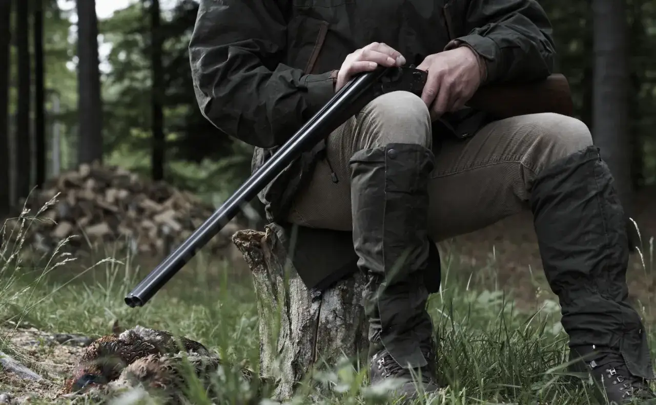 Myśliwy w lesie, z bronią i upolowanym ptakiem. Czy myśliwy może posiadać loftki? Tak, jeśli są to jego własne.