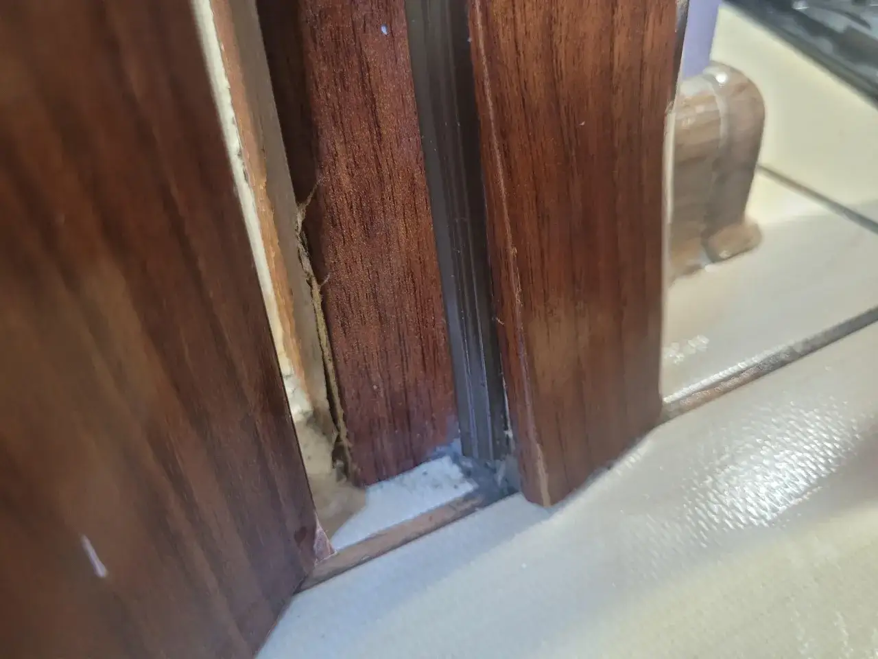 Uszkodzona, spuchnięta ościeżnica drzwiowa. Widoczne pęknięcia i wilgoć, wskazujące na potrzebę naprawy.