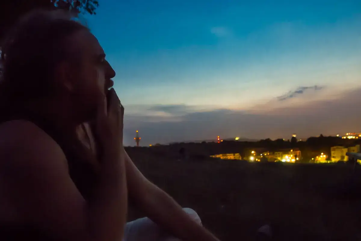 Zamyślony mężczyzna patrzy na nocne miasto. Myśli o tym, co odpisać na tęsknię, gdy niebo ciemnieje.