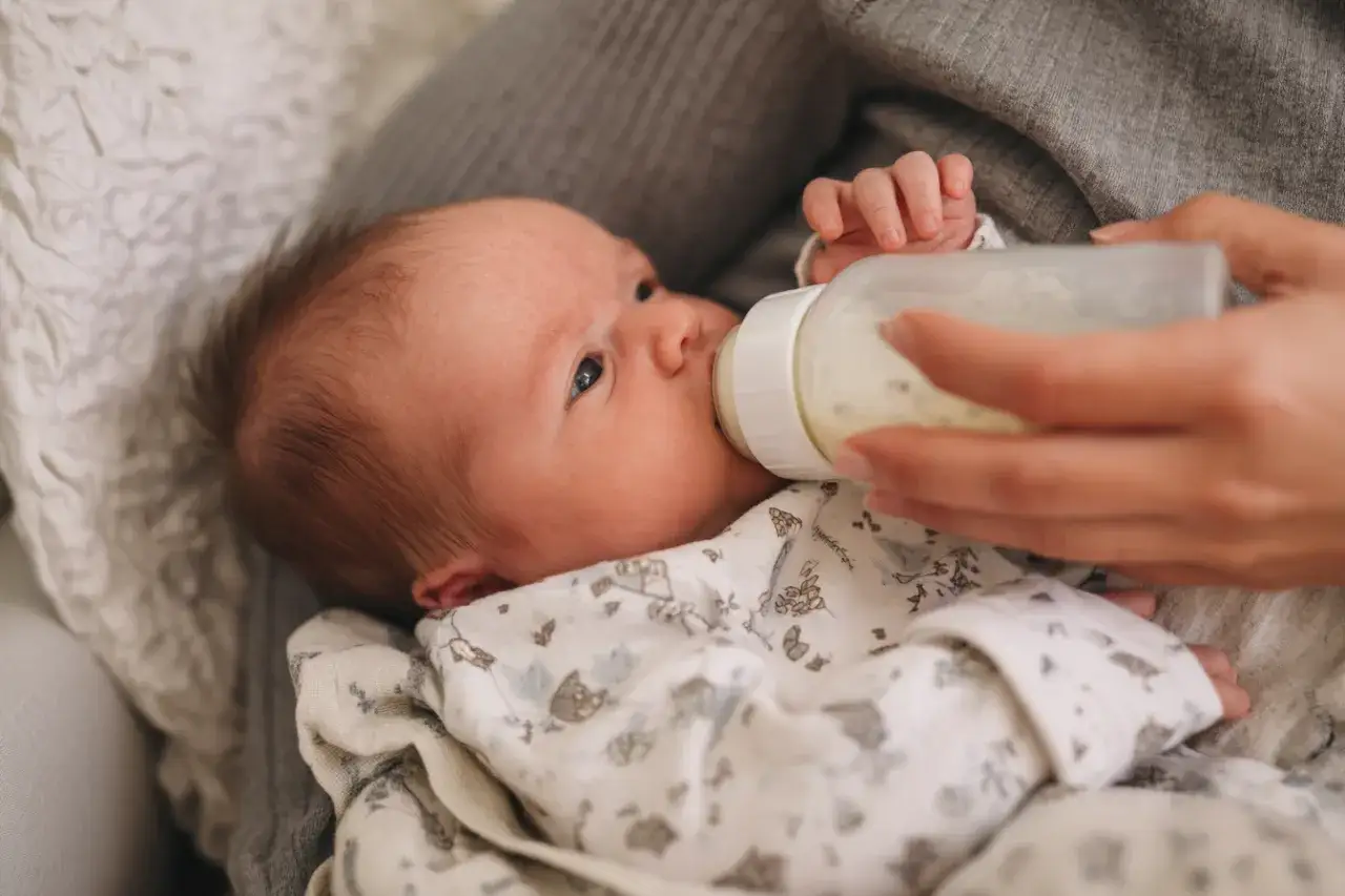 Mały głodom&oacute;r pije mleko modyfikowane z butelki.