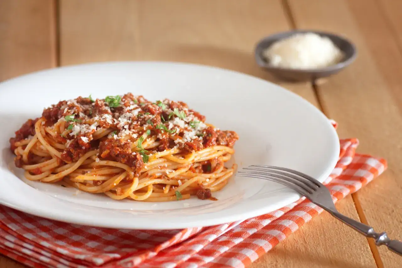 Porcja spaghetti z sosem bolońskim, posypana parmezanem. Zastanawiasz się, ile kalorii ma sos do spaghetti z mięsem mielonym?