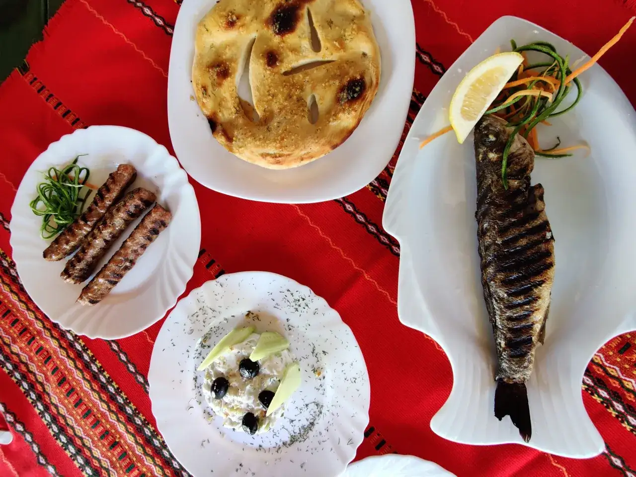 Co zjesc w Bułgarii? Grillowana ryba, kiełbaski, sałatka z oliwkami i chleb czosnkowy na tradycyjnym obrusie.
