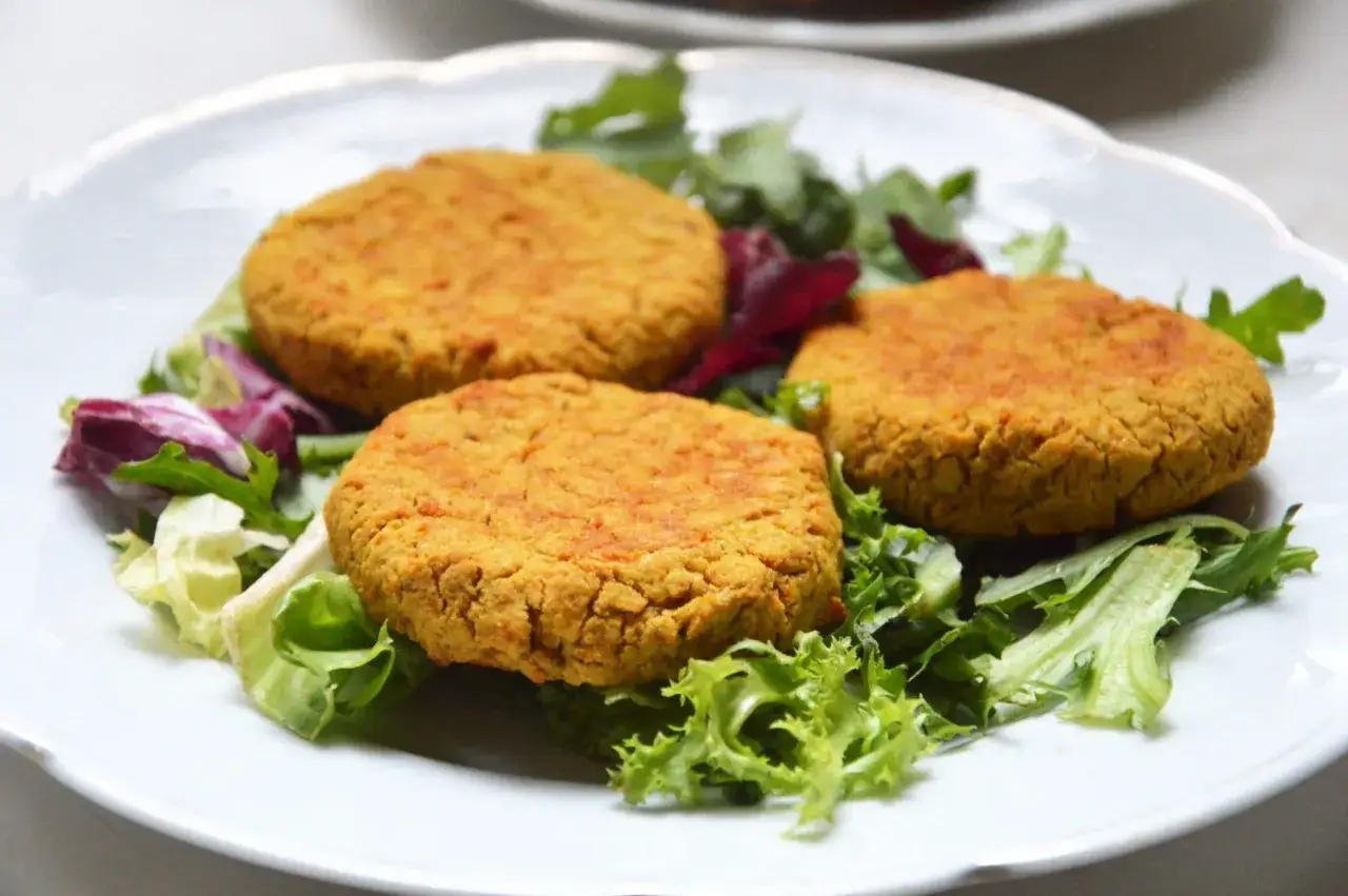 Trzy złociste kotleciki z ciecierzycy na talerzu z sałatką. Idealne co na obiad zamiast ryby, gdy masz ochotę na coś pysznego i zdrowego.