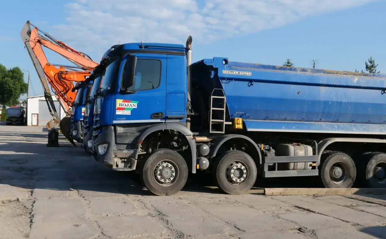 Błękitne wywrotki i koparka pomarańczowa. Zastanawiasz się, ile kosztuje tona żwiru? Te ciężarówki są gotowe do transportu.