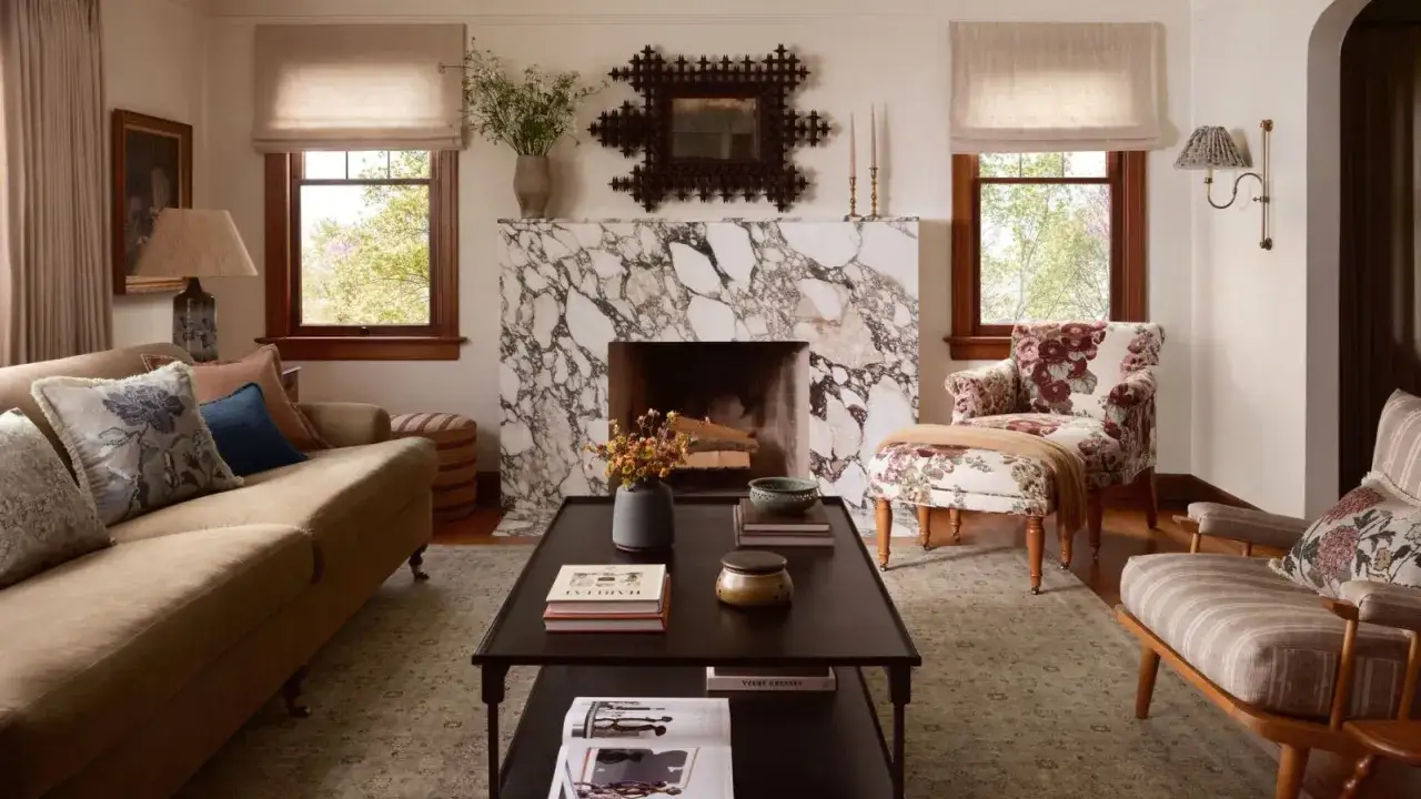 Jasne wnętrza inspiracje: przytulny salon z marmurowym kominkiem, beżową kanapą i kwiecistym fotelem.