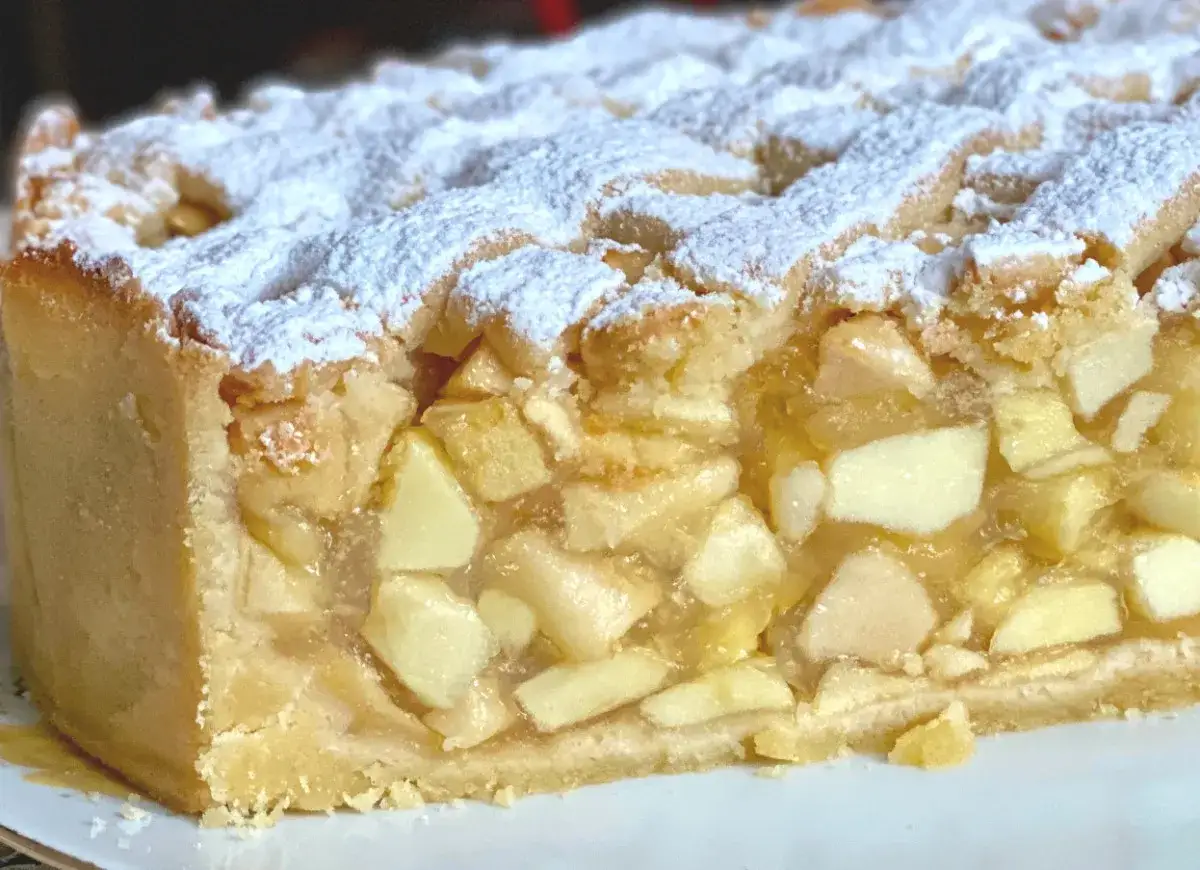 Szarlotka z widocznymi kawałkami jabłek, posypana cukrem pudrem. Chcesz wiedzieć, co zrobić, żeby jabłka w szarlotce były sztywne?