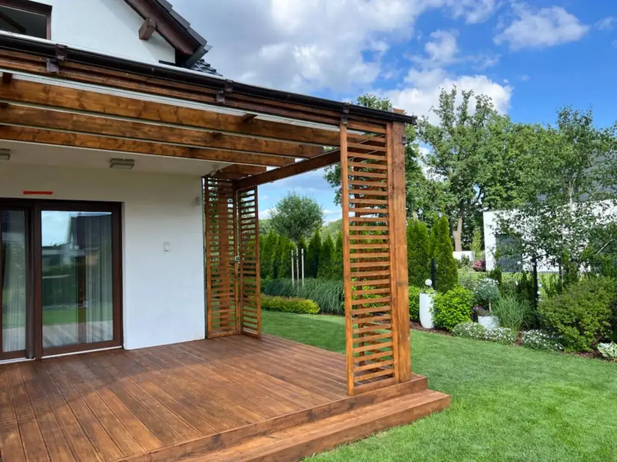 Piękny, świeżo odnowiony szlifowanie tarasu drewnianego. Wokół zadbany ogród z zieloną trawą i ozdobnymi krzewami.