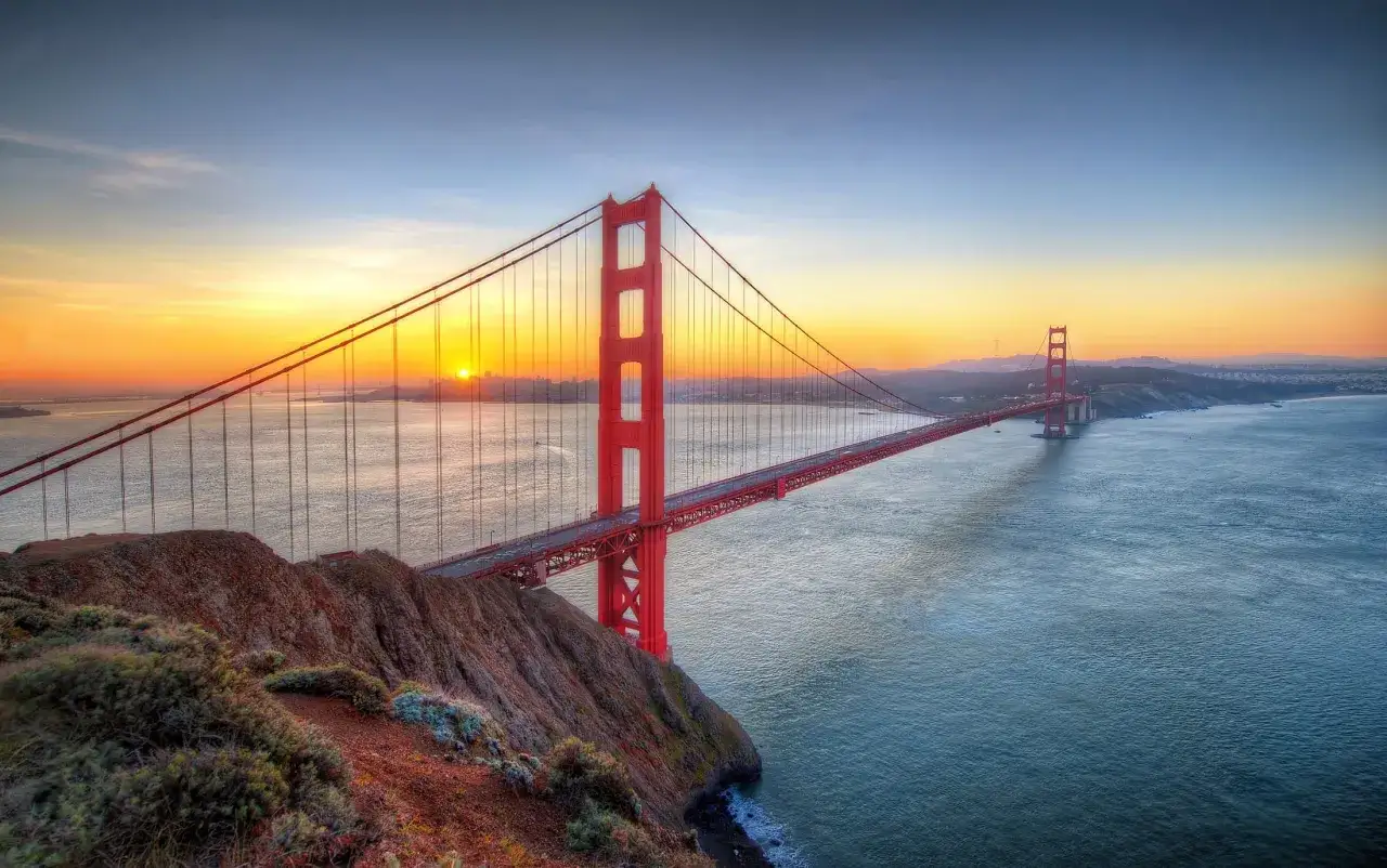 Zach&oacute;d słońca nad Zatoką San Francisco, z charakterystycznym czerwonym San Francisco mostem w tle.