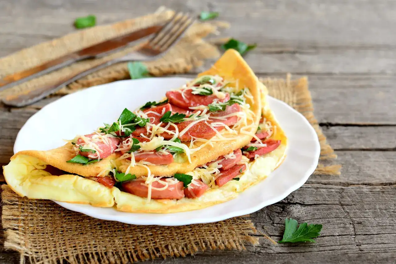 Puszysty omlet z kiełbasą i serem, posypany natką pietruszki. Idealne dania bezglutenowe przepisy na szybkie śniadanie.