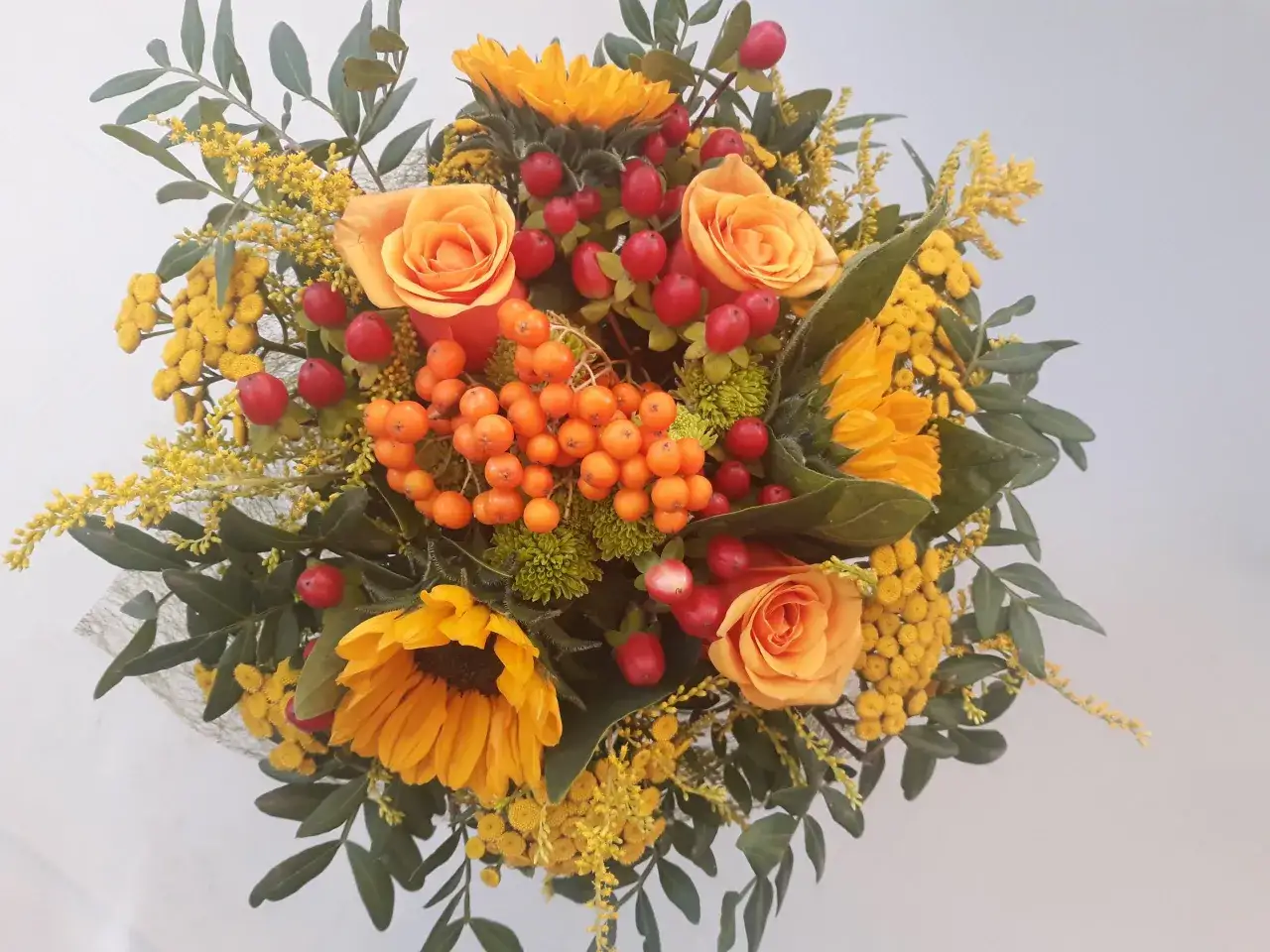 Jesienny bukiet z pomarańczowymi różami, słonecznikami i koralikami jarzębiny.