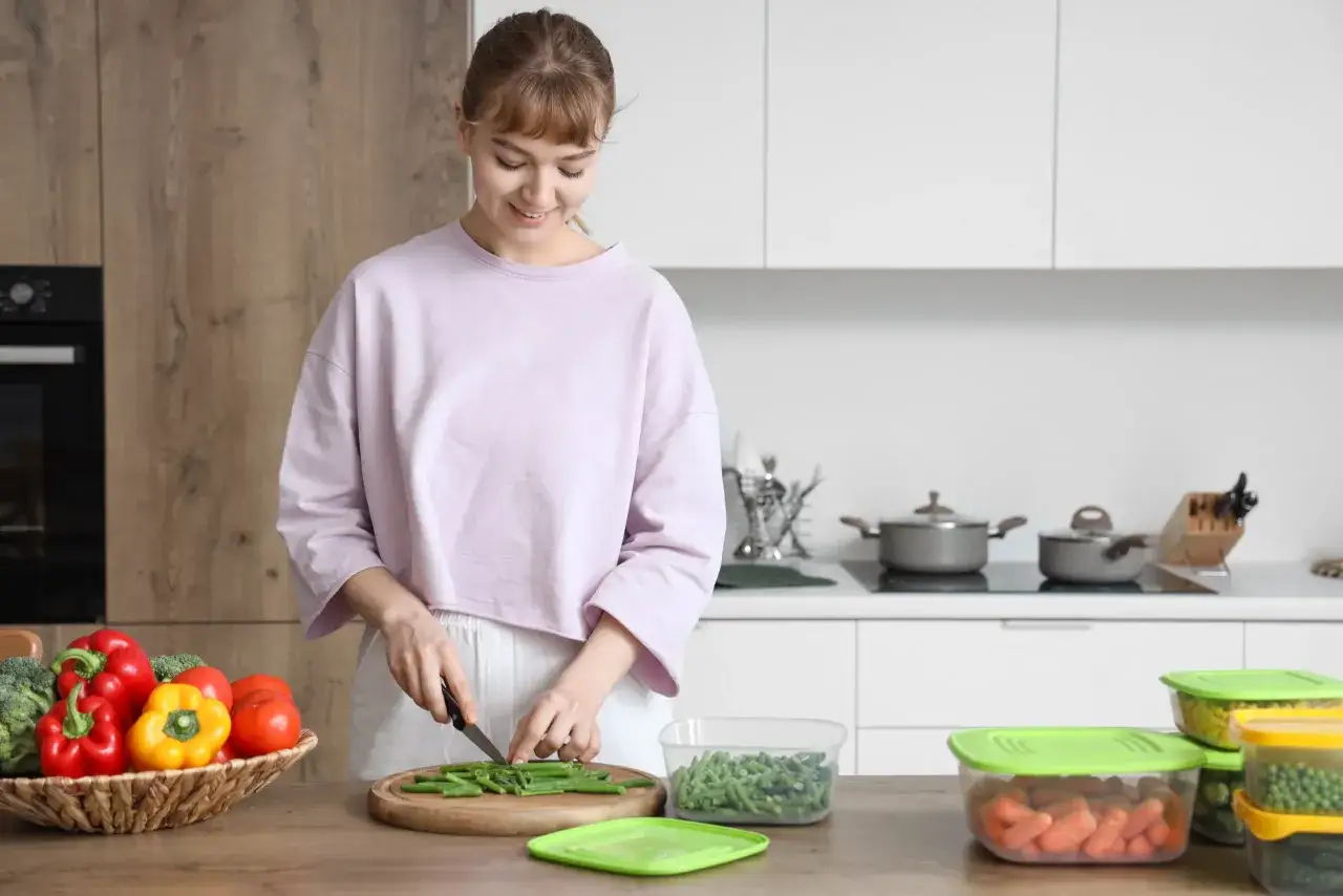 Młoda kobieta kroi fasolkę szparagową, przygotowując posiłek. To przykład, co to jest kuchnia wegańska &ndash; pełna świeżych warzyw i zdrowych składnik&oacute;w.