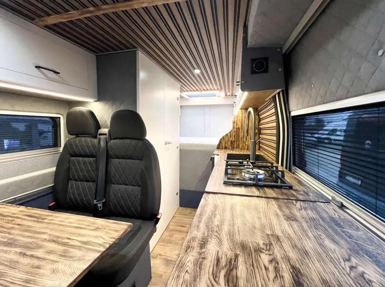 Wnętrze kamper van z wygodnymi siedzeniami, aneksem kuchennym i drewnianym wykończeniem.