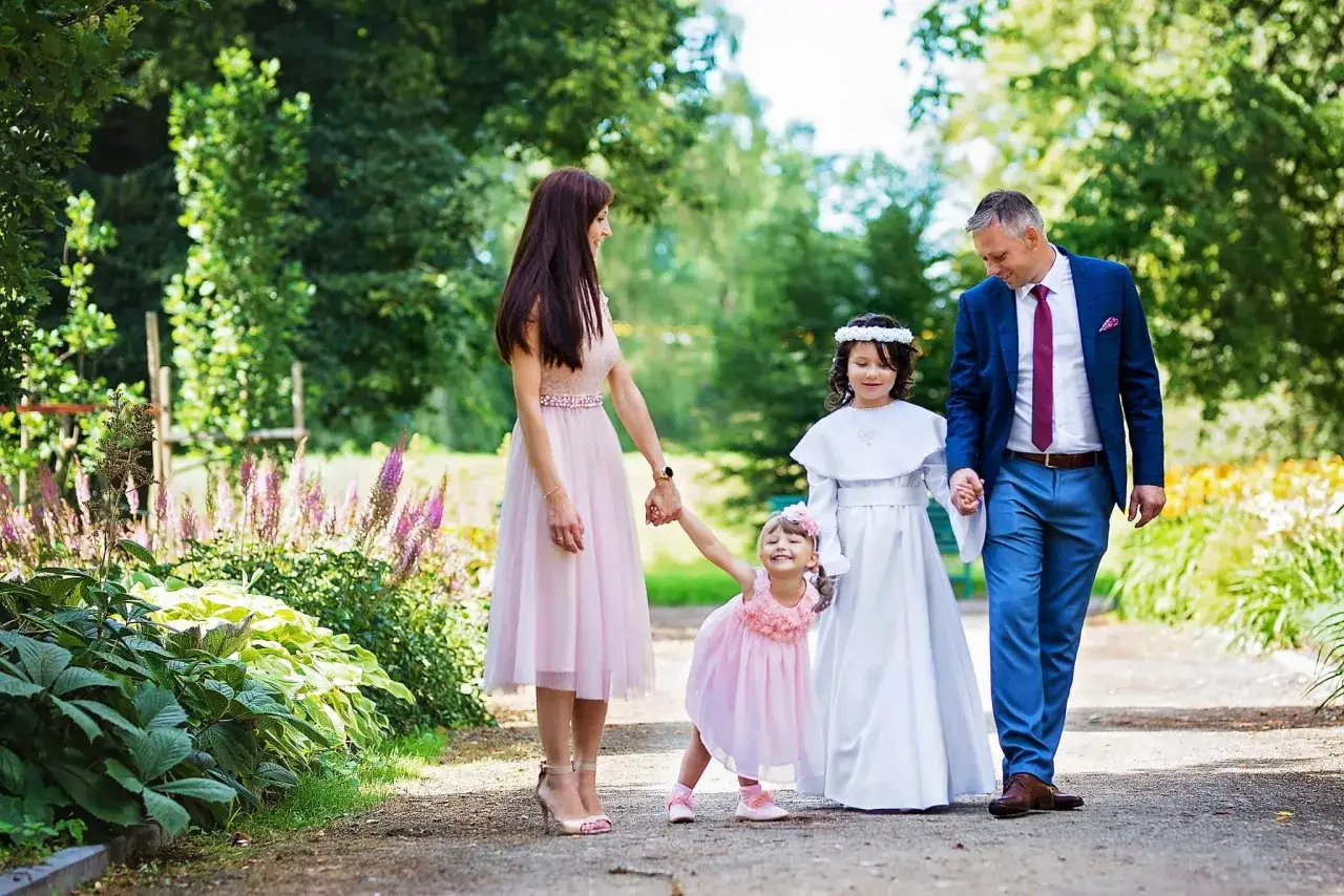 Rodzina spaceruje po parku. Rodzice trzymają za ręce dwie córki w strojach komunijnych. Zastanawiasz się, ile kosztuje fotograf na komunię?