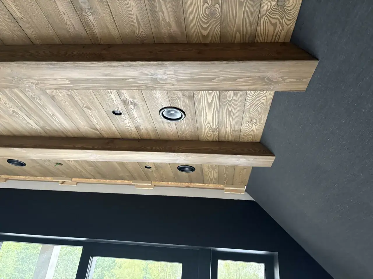 Drewniany sufit z belkami, ocieplony i wykończony deskami, z wbudowanymi punktami świetlnymi.