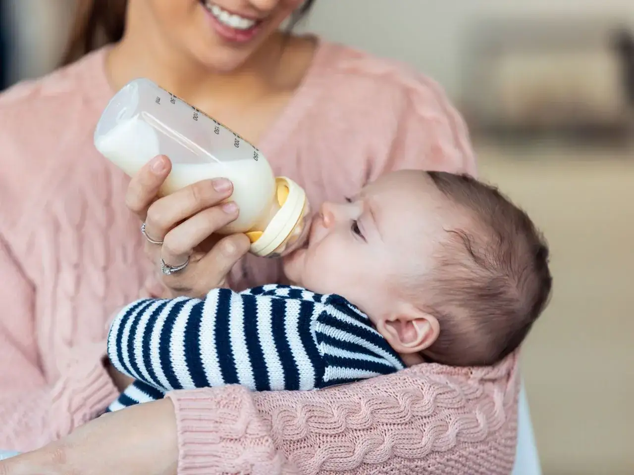 Uśmiechnięta mama karmi dziecko butelką. Długość karmienia butelką zależy od apetytu malucha.