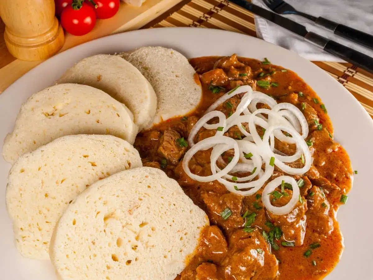 Gulasz z wołowiny z knedlikami, idealny, by dowiedzieć się, co warto zjeść w Czechach. Danie ozdobione cebulą i szczypiorkiem.