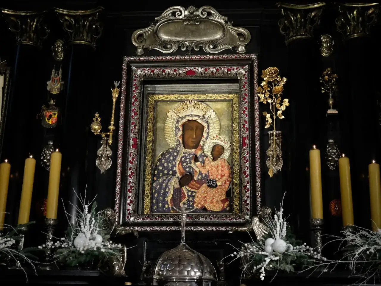 Obraz Matki Boskiej Częstochowskiej w ozdobnej ramie, otoczony świecami i świątecznymi dekoracjami. Godziny odsłonięcia obrazu na Jasnej Górze.