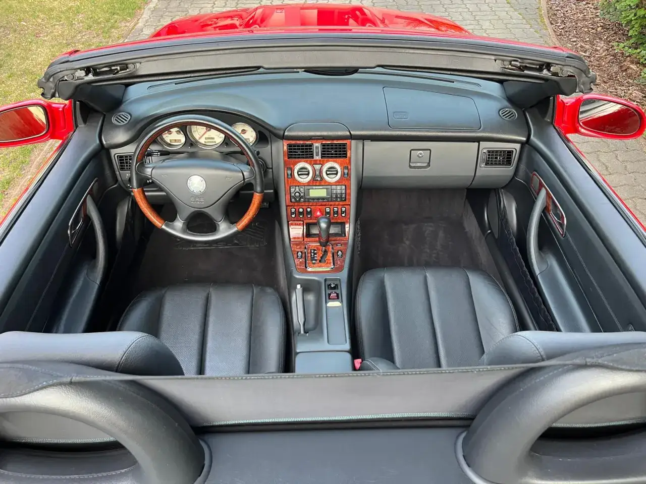 Wnętrze czerwonego Mercedesa Benz SLK z czarną skórzaną tapicerką i drewnianymi wstawkami.