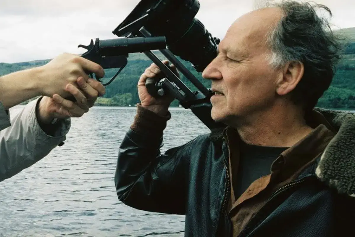 Werner Herzog z kamerą i pistoletem w ręku, gotowy do uchwycenia surowego piękna natury w swoich filmach.