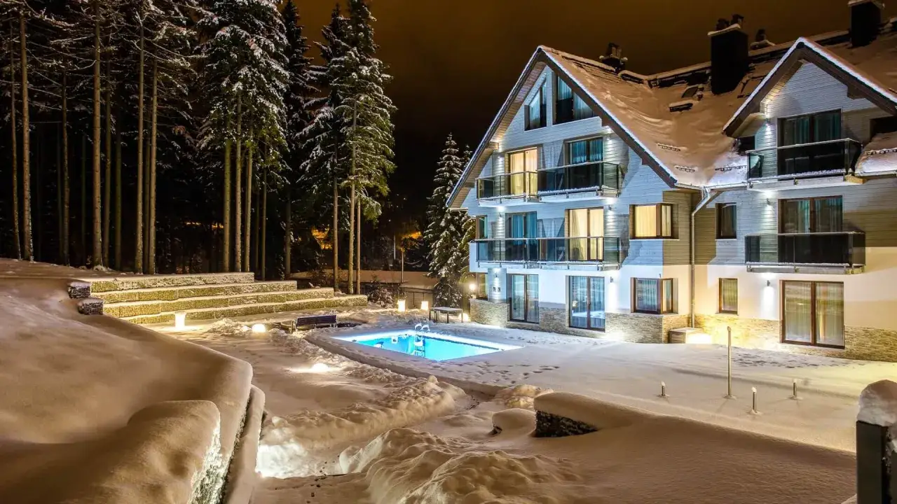 Nowoczesny hotel z basenem w Szklarskiej Porębie, otoczony ośnieżonym lasem. Woda w basenie lśni błękitem, kontrastując z zimową scenerią.