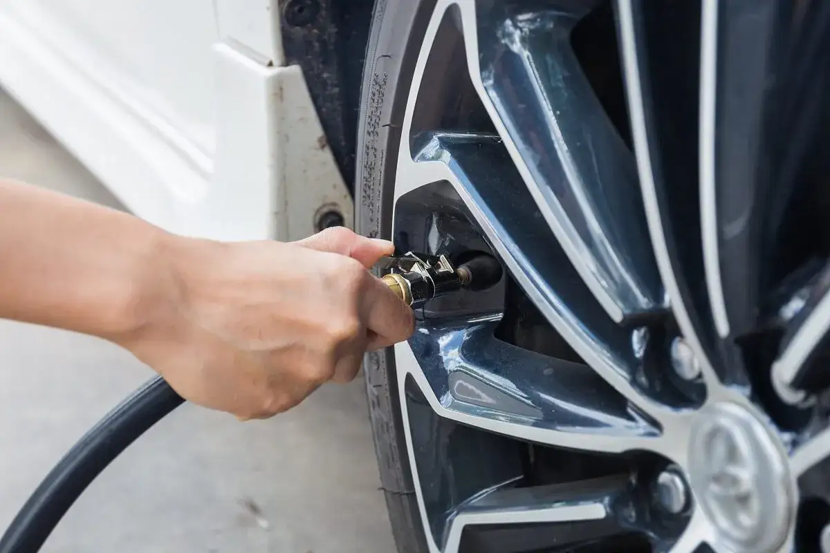 Ręka podłącza pompkę do wentyla, by uzupełnić powietrze. Zapobiega to **niskie ciśnienie w oponach** i zapewnia bezpieczną jazdę.