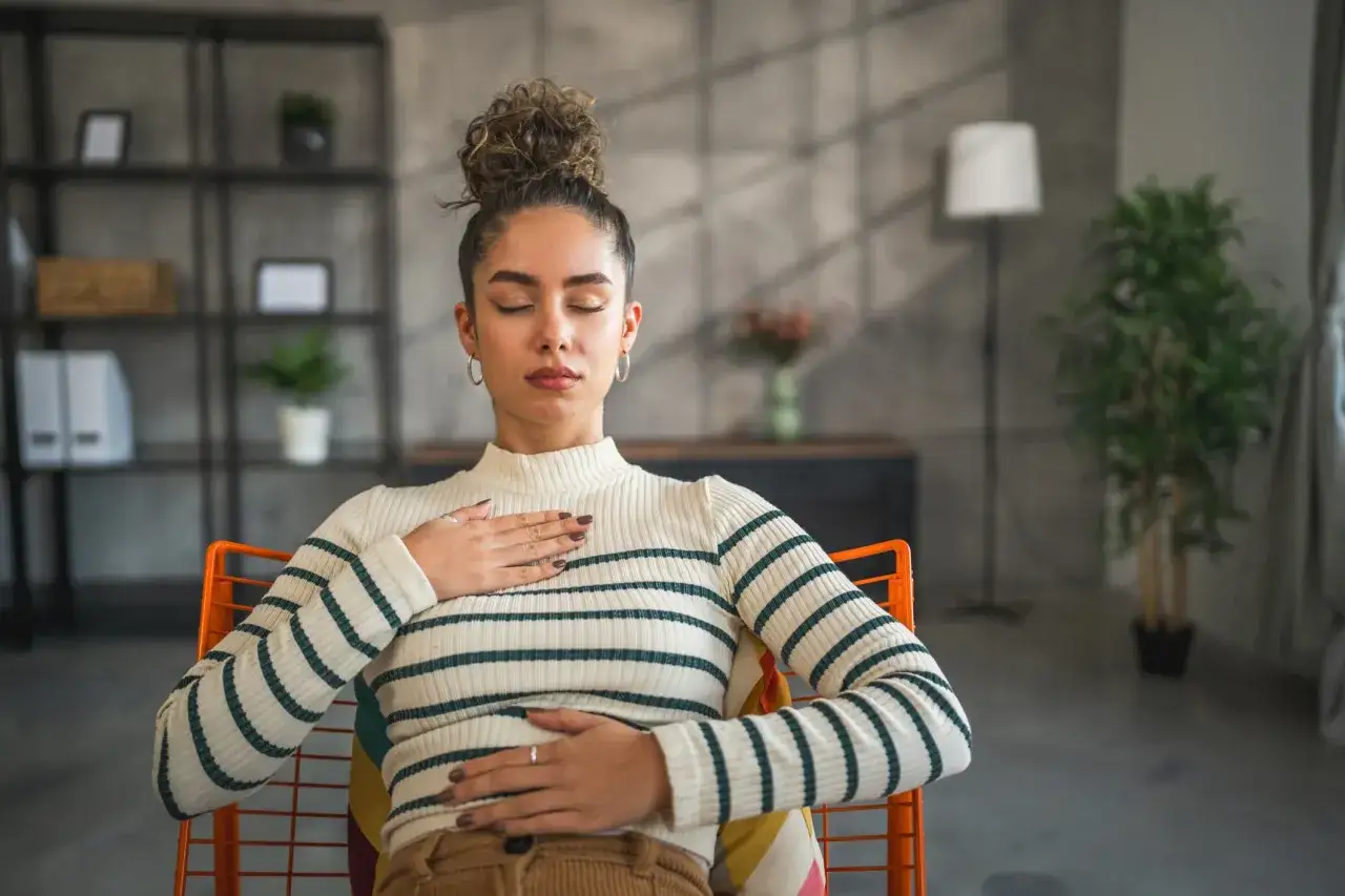 Kobieta z zamkniętymi oczami, praktykująca oddychanie przeponowe, z dłońmi na klatce piersiowej i brzuchu.
