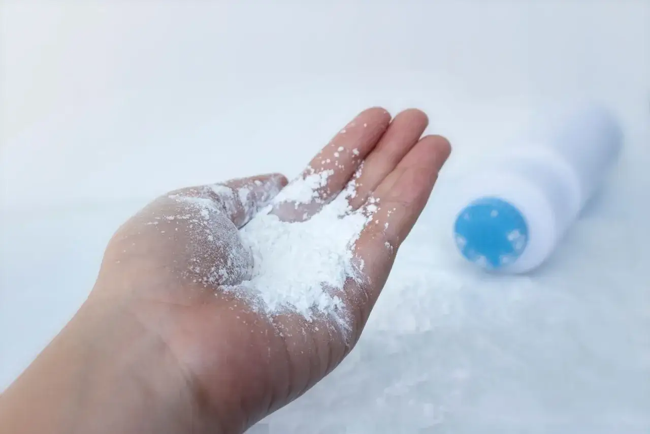 Dłoń z białym pudrem, obok leży buteleczka. To talk, kt&oacute;ry pomaga zachować suchość.