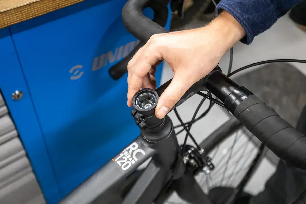 Dłoń dokręca śrubę w mostku, regulując ustawienie kierownicy w rowerze szosowym.